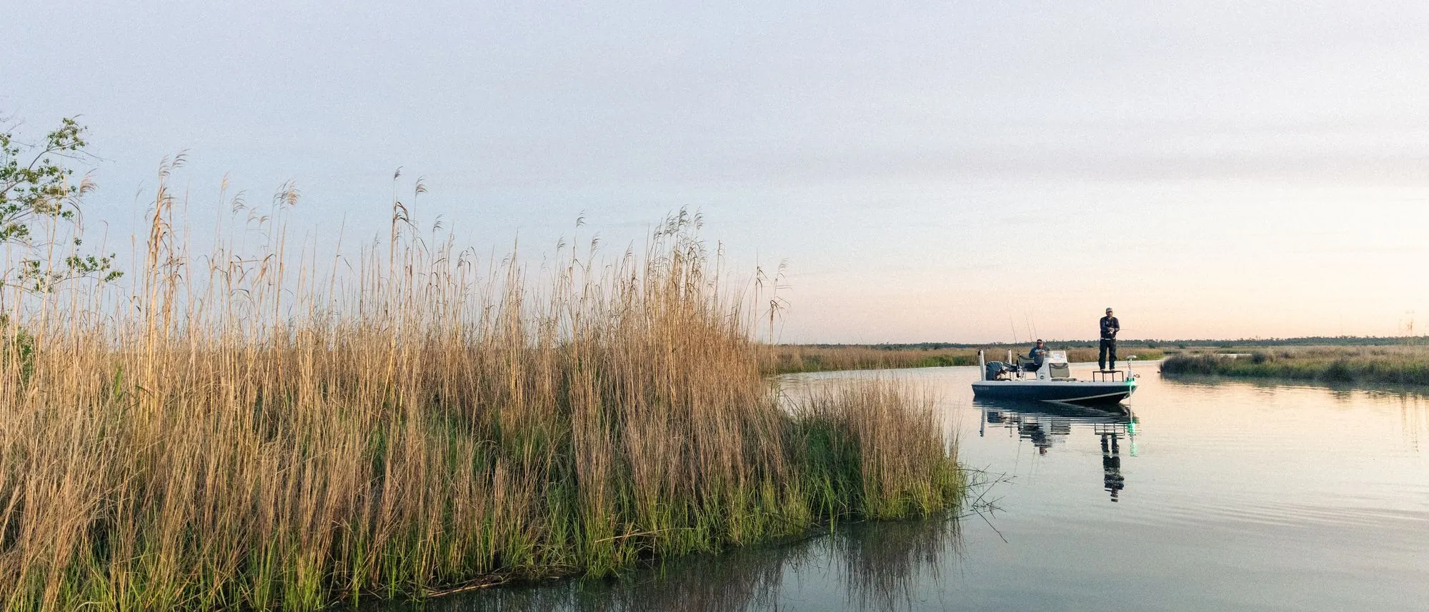 Two anglers fishing from a bay boat in a marsh creek at dusk